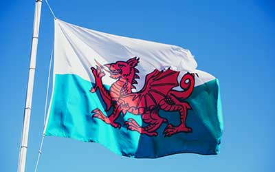A Welsh flag flying in the wind with blue skies behind