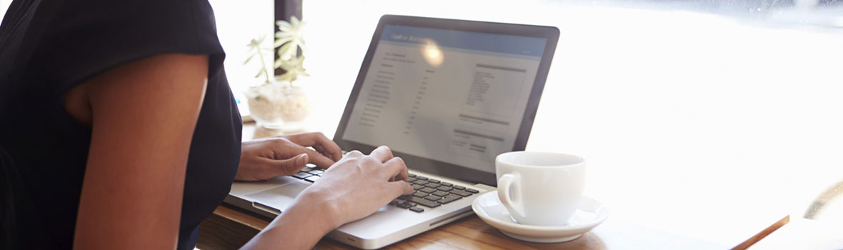 A person typing at a laptop computer on a desk next to a coffee cup