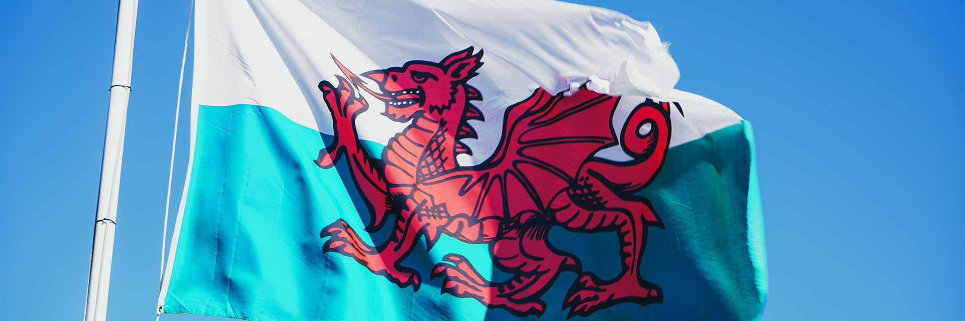 A Welsh flag flying in the wind against blue skies